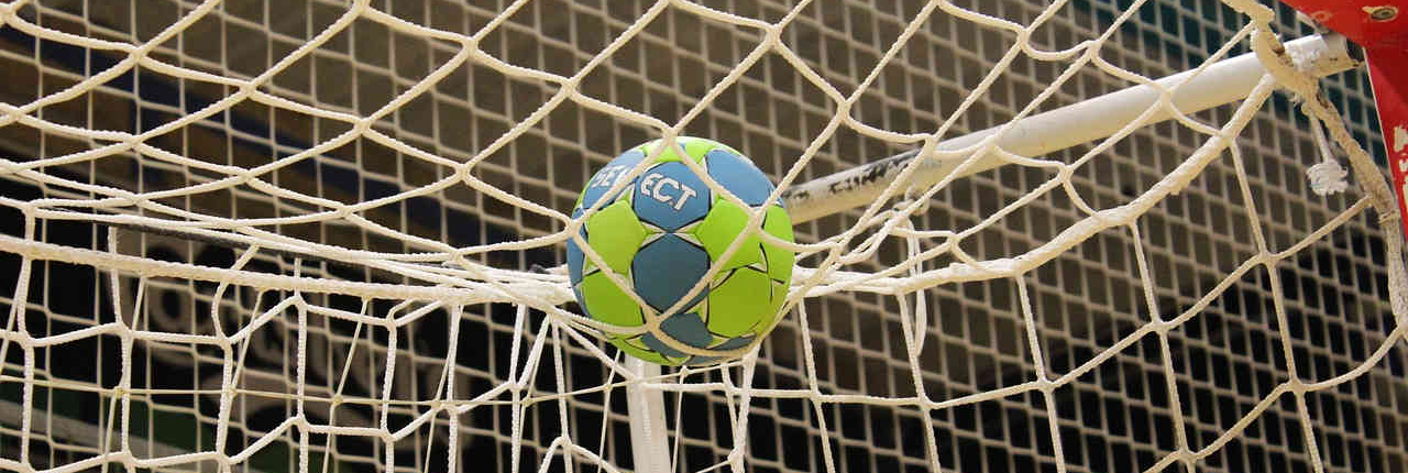 Ein grün-blauer Handball liegt oben auf dem weißen Tornetz. Die Männer-Handball WM 2025 verspricht spannende Spiele. Bei Tippevent.de kannst du auf die WM sowie auf viele andere Sportarten wie Handball, Fußball und Basketball wetten und deine Tipps mit anderen teilen.